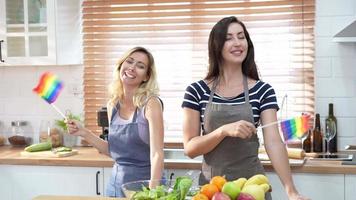 contento caucásico lgbt pareja, lesbiana participación y ondulación arco iris lgbt orgullo bandera juntos en el cocina a hogar. diversidad de lgbt relaciones alegre homosexual Pareja. video