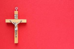 Crucifix christian wooden cross on red background. Catholic symbol. Flatlay, top view, lay out, isolated. Pray for God, faith in Jesus Christ and believe religion concept. Closeup