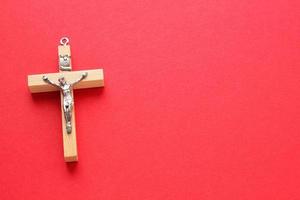 Crucifix christian wooden cross on red background with copy space. Catholic symbol. Flatlay, top view, lay out, isolated. Pray for God, faith in Jesus Christ and believe religion concept. Closeup photo