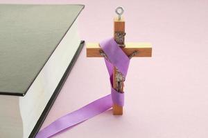 cristiano religioso de madera cruzar crucifijo con Violeta cinta y Biblia libro en púrpura antecedentes. católico religión símbolo. bueno viernes, prestado estación, palma domingo, ceniza miércoles y santo semana concepto foto