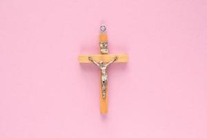 Crucifix christian wooden cross on pink background. Catholic symbol. Flatlay, top view, lay out, isolated. Pray for God, faith in Jesus Christ and believe religion concept. Closeup photo