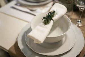 Christmas dinner, white plates and a napkin with a branch of a Christmas tree on the table photo