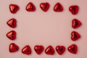 A frame of many shiny heart-shaped candies wrapped in foil on a pink background photo