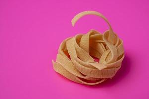 Raw tagliatelle nest on pink background, pasta nest, egg paste nest photo