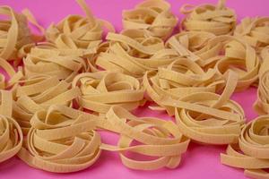 Raw tagliatelle , nest pasta, Egg pasta nests lying in a pattern on a pink background photo