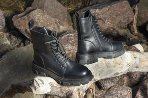 Leather black women's rough boots with thick soles standing on a piece of wood against a background of stones photo