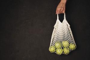 A woman's hand holds a string bag with green apples on a dark textured background photo