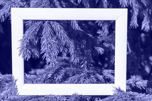 An empty fotoframe on a background of spruce branches with a place to copy, photo tinted in Very peri color