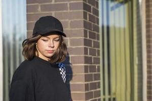 Cute trendy cheeky Caucasian girl dressed in a trendy black baseball cap and black sweatshirt photo