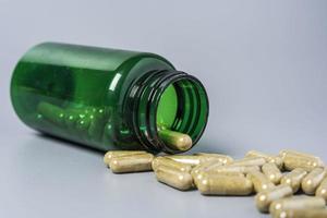 Capsules with vitamins and minerals are poured out of the jar on a gray background. Close-up photo