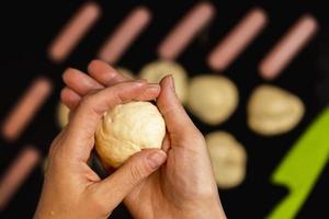 Women's hands sculpt a piece of dough for cooking sausages in dough, cooking hot dogs photo