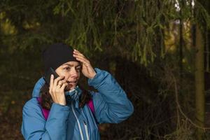 A tourist girl is talking on the phone in the forest, a tourist got lost in the forest. Call for help photo