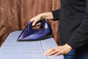 Women's hands hold an iron and iron clothes on an ironing board at home, lifestyle photo
