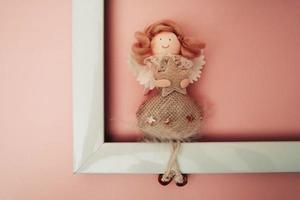 a figure of a funny angel sitting on the edge of an empty white photo frame