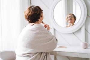 sonriente medio Envejecido más Talla mujer haciendo maquillaje cerca espejo a hogar foto