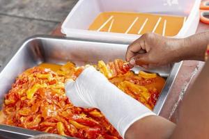 Hands of a merchant wearing white rubber gloves plugging the pork into the wood sticks to make grilled pork. photo
