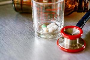 Closeup capsules and tablet in a glass with Medical stethoscope on aluminium plate photo