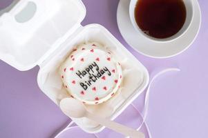 A small bento cake in eco-packaging with a wooden spoon next to a cup of tea on a purple background photo