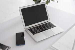 Laptop on a white table next to the phone photo