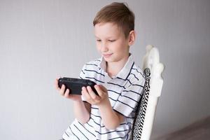 The boy is sitting on a chair and playing a video game console photo