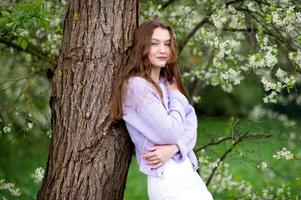 A young girl in a sweater next to white flowers on a tree photo