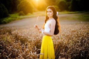 A girl in a yellow skirt stands in a field against the background of the setting sun photo