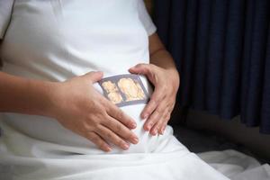 Image of Asian pregnant smiling woman sitting and posing while showing ultrasound scans, look into the camera photo