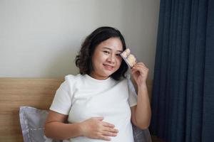 Image of Asian pregnant smiling woman sitting and posing while showing ultrasound scans, look into the camera photo