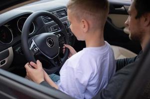 Dad and a cute boy hold the steering wheel of a car with their hands photo