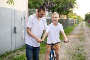 A cute boy in a white T-shirt rides a bike with his dad and laughs. photo