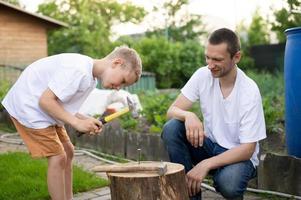 Dad teaches his son to hammer nails into a tree photo