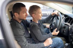 papá muestra su pequeño hijo cómo a conducir un coche foto