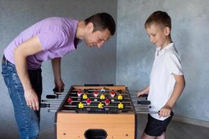 Cute boy playing table football with his emotional dad in the room photo