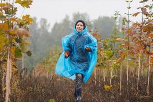 A boy runs in a raincoat near the trees photo