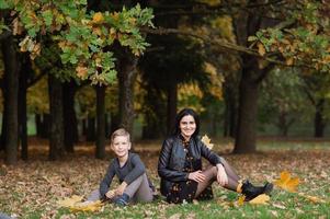 un niña y un chico son sentado en el suelo y lanzando otoño hojas foto