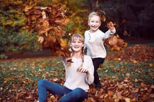 Happy girl and boy toss yellow autumn leaves in the forest photo