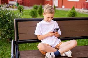 The boy is sitting on a bench and looking at the phone photo