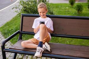 el chico es sentado en un banco y mirando a el teléfono foto