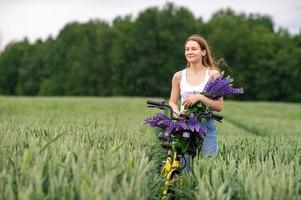 A cute girl is standing with a bouquet of lupines in a field near a bicycle photo