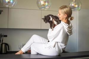 An emotional woman holds a pet gray cat in her arms while sitting on a table photo