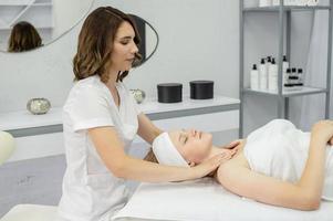 un cosmetóloga masajes el collar área. el niña es acostado con su ojos cerrado foto