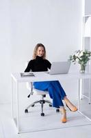 The girl works in a white office with a laptop and flowers on the table photo