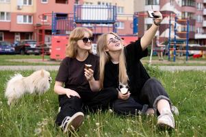 dos gracioso muchachas son comiendo hielo crema y jugando con un pomeranio perro. tomando selfies foto