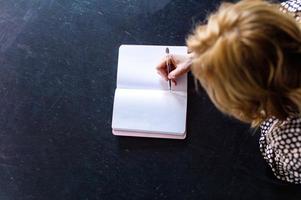 On a black background there is a notebook in which a person with a pen in his hands makes a note photo