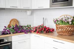 A large number of tulips of different colors lies on the table in the kitchen. Flowers in the sink photo