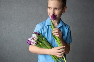 A cute boy is holding a bouquet of colorful tulips and smelling the flower. mother's day gift photo