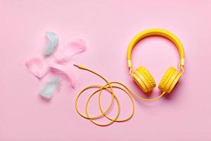 Yellow headphones and soft feathers on pink background. ASMR Stress-relieving sounds concept, flat lay photo