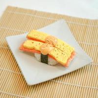 two pieces of sushi with egg and crab stick on top in a white plate photo