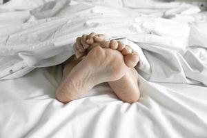 Couple feet under sheets on the bed at home. photo