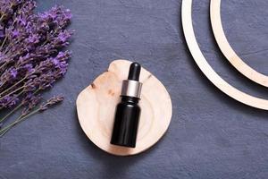 Dropper bottle with lavender flowers and wooden podium on dark background. Wellness flat lay concept. photo